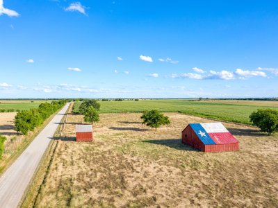 An abandoned old barn with the symbol of Texas painted on the roof sits in a rural area of the state, framed by farmland.